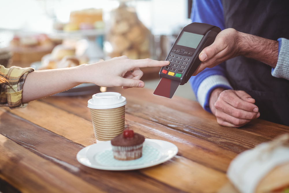 Henkilö maksaa tilaustansa kahvilassa pankkikortilla. 